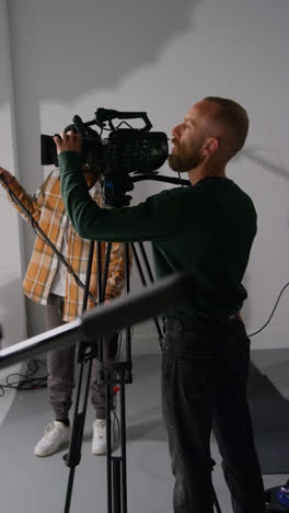 Vertical-Video-Of-Male-Sound-Recordist-And-Camera-Operator-Working-On-Film-Set-Shooting-Movie-Or-Video-In-Studio